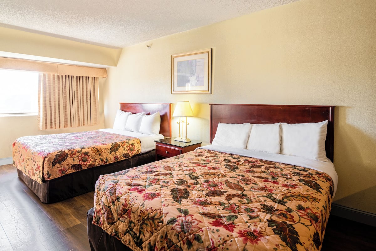 A hotel room with two beds, each with floral bedding, a nightstand, a lamp, and a framed picture on the wall.