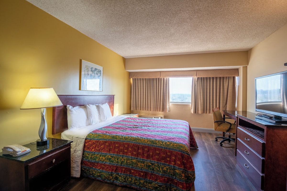 A hotel room with a bed, a desk with a lamp, a chair, a TV, and a window with curtains.