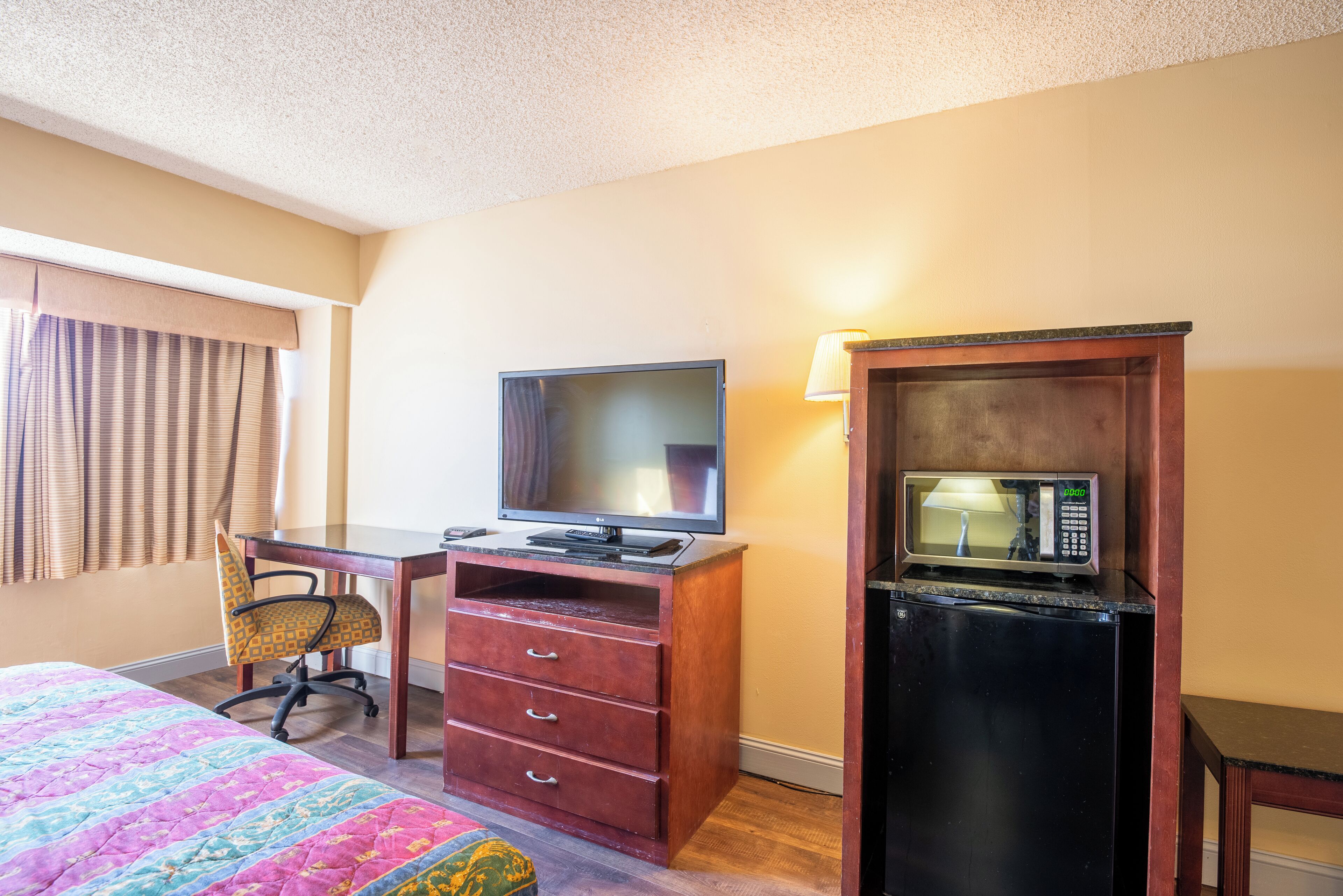 Una habitación de hotel con cama, escritorio con televisor, microondas y silla.