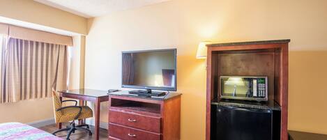 Una habitación de hotel con cama, escritorio con televisor, microondas y silla.