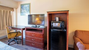 Ein kleines Hotelzimmer mit einem Holztisch, einem Fernseher, einer Mikrowelle, einem gemusterten Sessel und einem gemusterten Sofa.