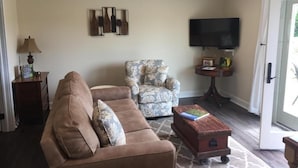 A living room with a brown sofa, a patterned armchair, a small wooden coffee table, and a television on the wall. - Vineyard Villa overlooking 40 acres of Vineyards in Ohio Wine Country (Geneva)