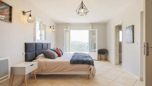 A bedroom with a bed, bedside table, and a view of the outdoors. - Villa Spacieuse Avec Piscine Proche de la Promenade Des Anglais (Nice)