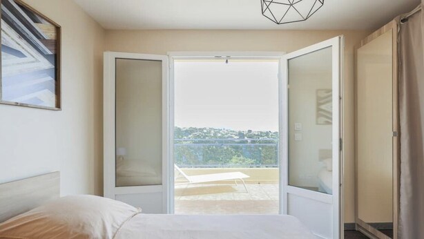 A bedroom with a bed, a window, and a balcony with a view of the city. - Villa Spacieuse Avec Piscine Proche de la Promenade Des Anglais (Nice)