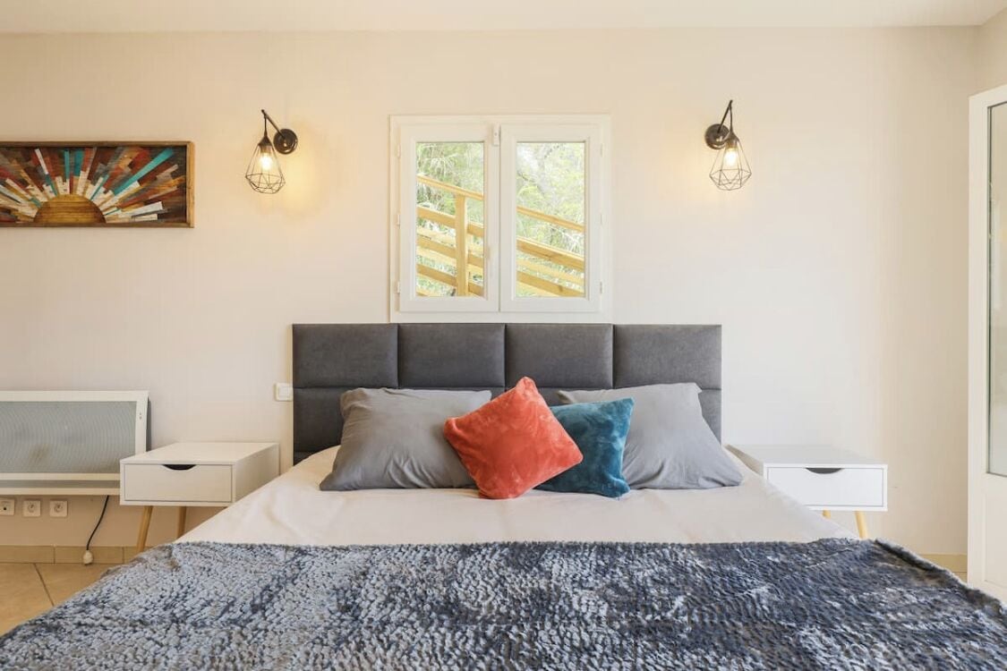 Une chambre à coucher comprenant un lit, deux tables de chevet, une fenêtre avec vue et une œuvre d’art accrochée au mur.