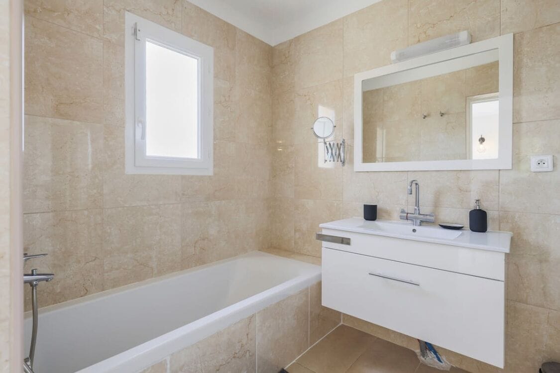 A modern bathroom with a bathtub, a vanity with a mirror, and a window.