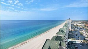 Un hotel frente a la playa con una hilera larga de edificios a lo largo de la costa, vista despejada al océano y un estacionamiento con coches.