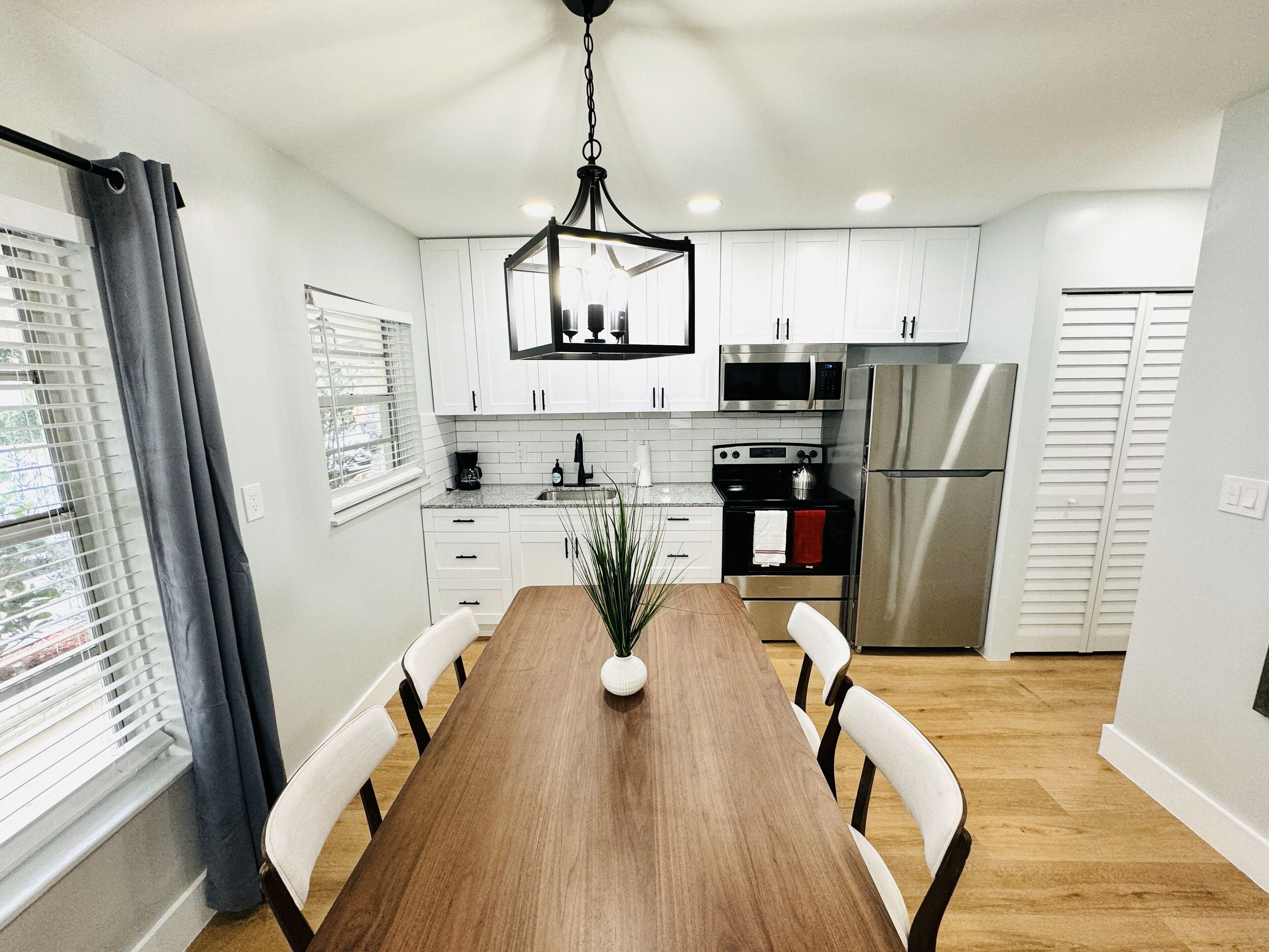A modern kitchen with white cabinets, stainless steel appliances, and a wooden dining table with chairs.