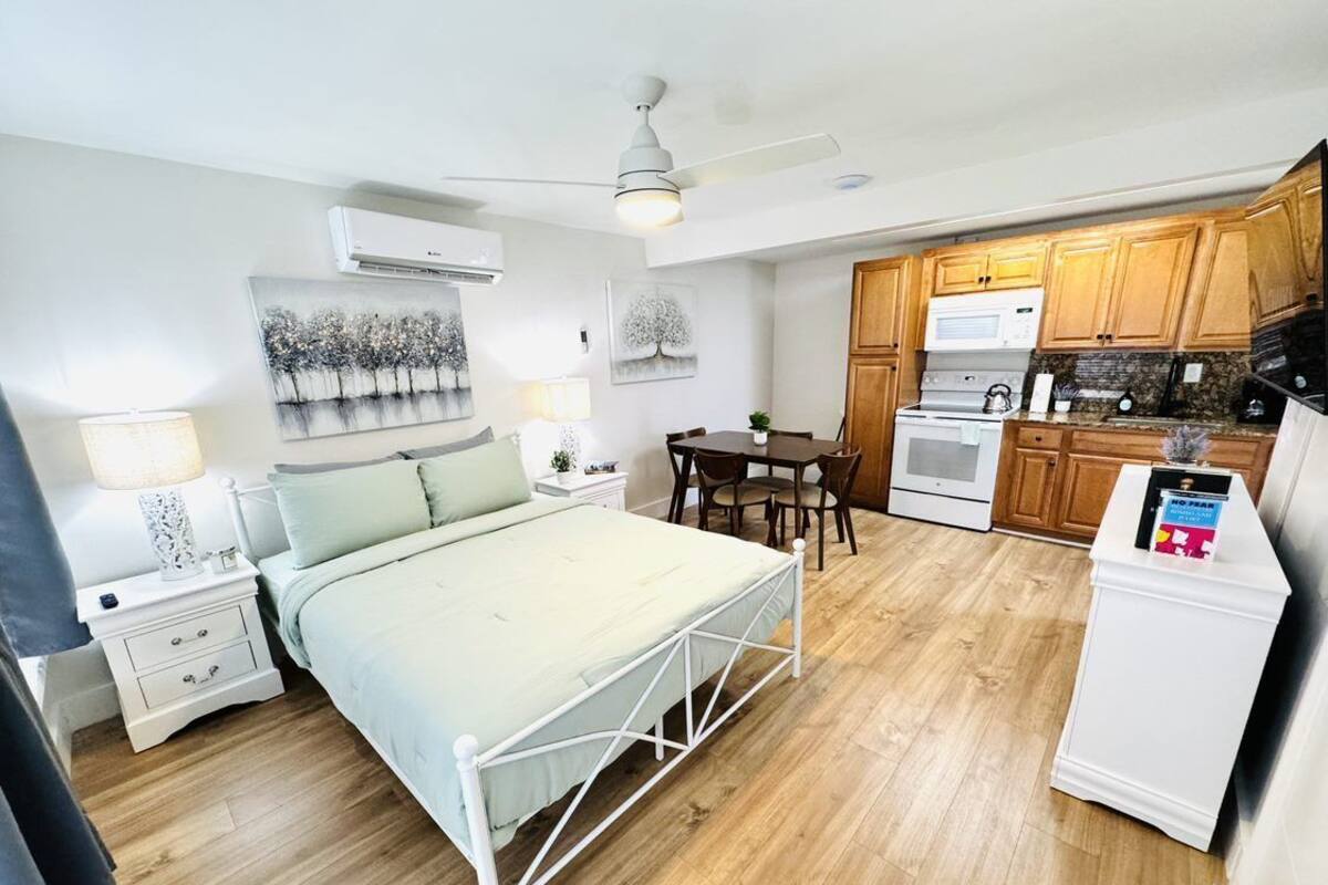 Ein gemütliches Schlafzimmer mit Bett, Nachttischen und einem kleinen Schreibtisch. Angrenzend befindet sich eine Küchenzeile mit Herd, Mikrowelle und Schränken.