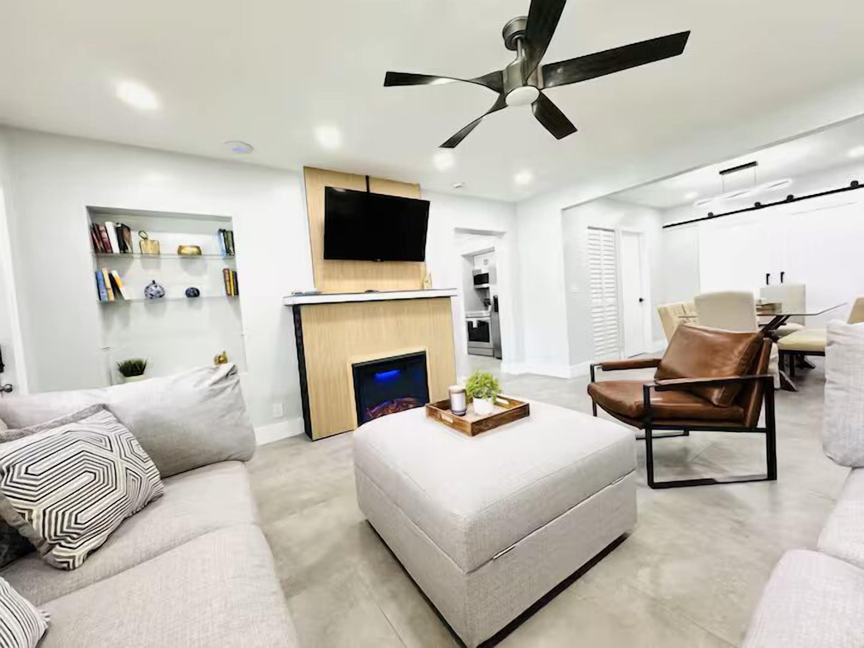 A modern living room with a sofa, ottoman, and a flat-screen TV mounted above a fireplace.