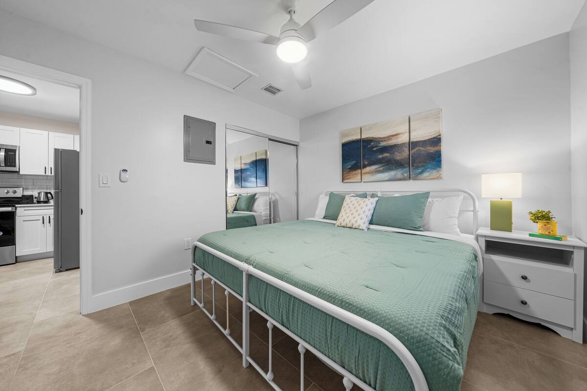 Ein modernes Schlafzimmer mit einer grünen Bettdecke, einem Nachttisch mit Lampe und einem Bild an der Wand.