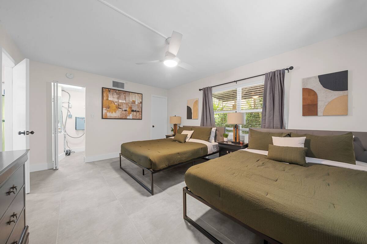 Ein Hotelzimmer mit zwei Betten, einem Deckenventilator, Kunstwerken an den Wänden und einem mit Vorhängen versehenen Fenster.