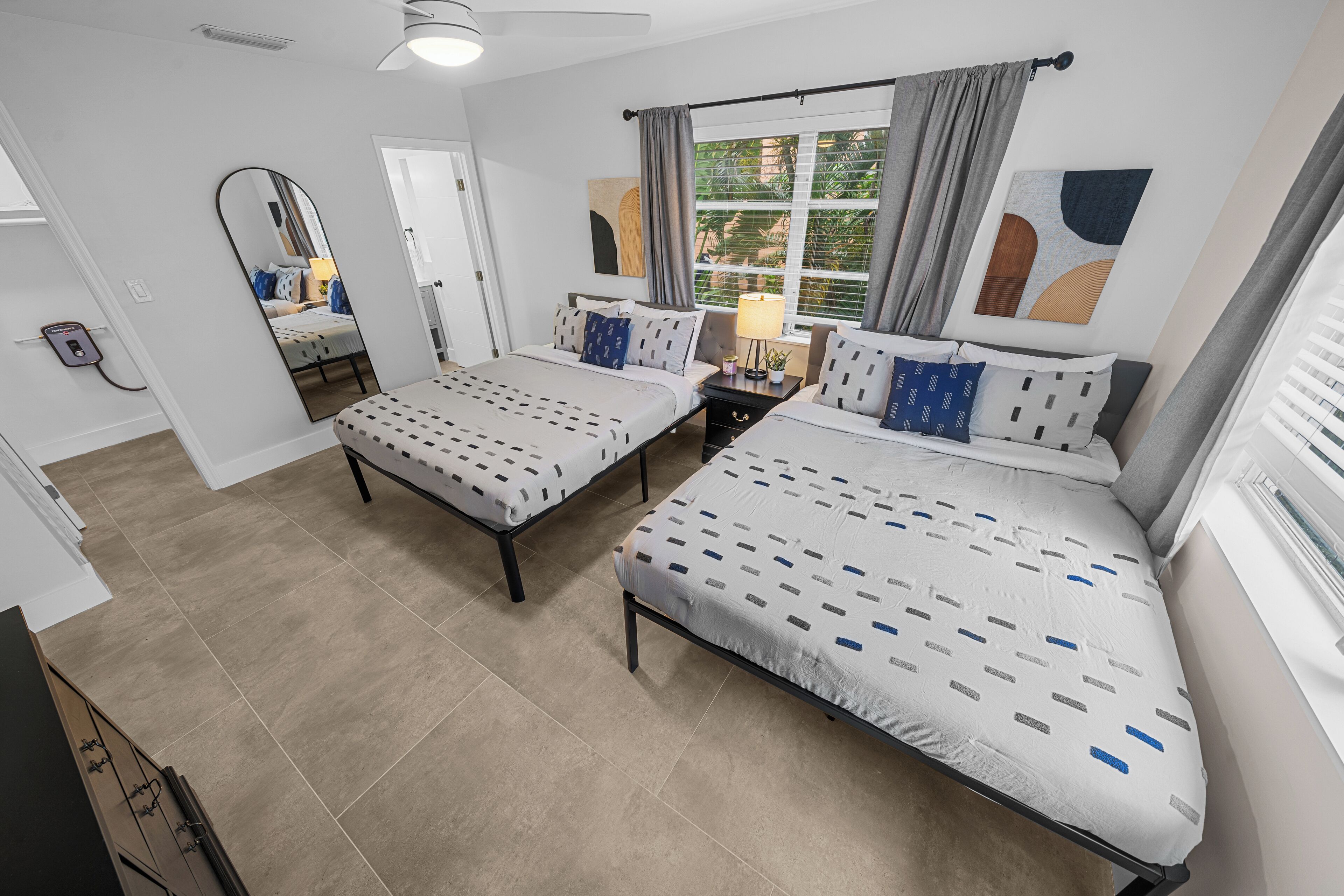 A modern bedroom with two beds, a large mirror, and a window with curtains.