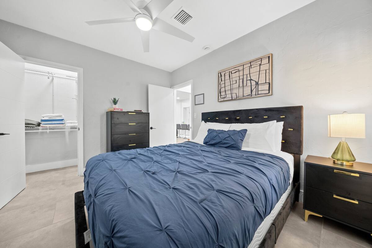 Ein Schlafzimmer mit Bett, Nachttischen, Deckenventilator, Kleiderschrank und einem an der Wand befestigten Kunstwerk.