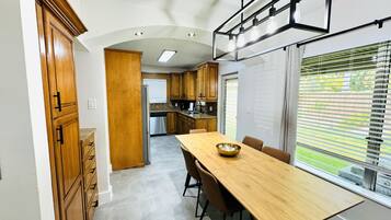 A modern kitchen with wooden cabinets, a stainless steel refrigerator, and a dining area with a long wooden table and chairs.