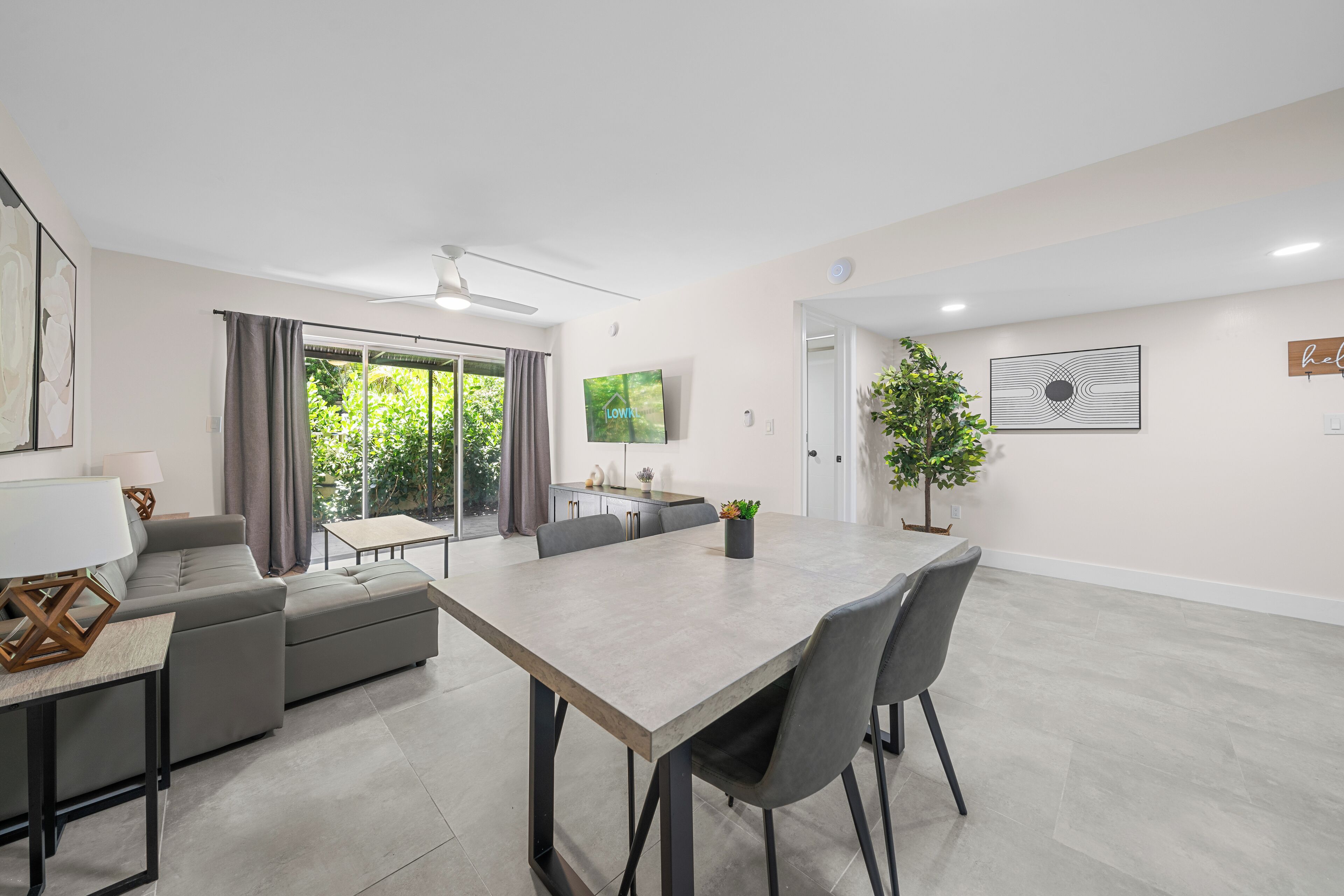 A modern living room with a dining area, a sofa, a TV, and a ceiling fan.