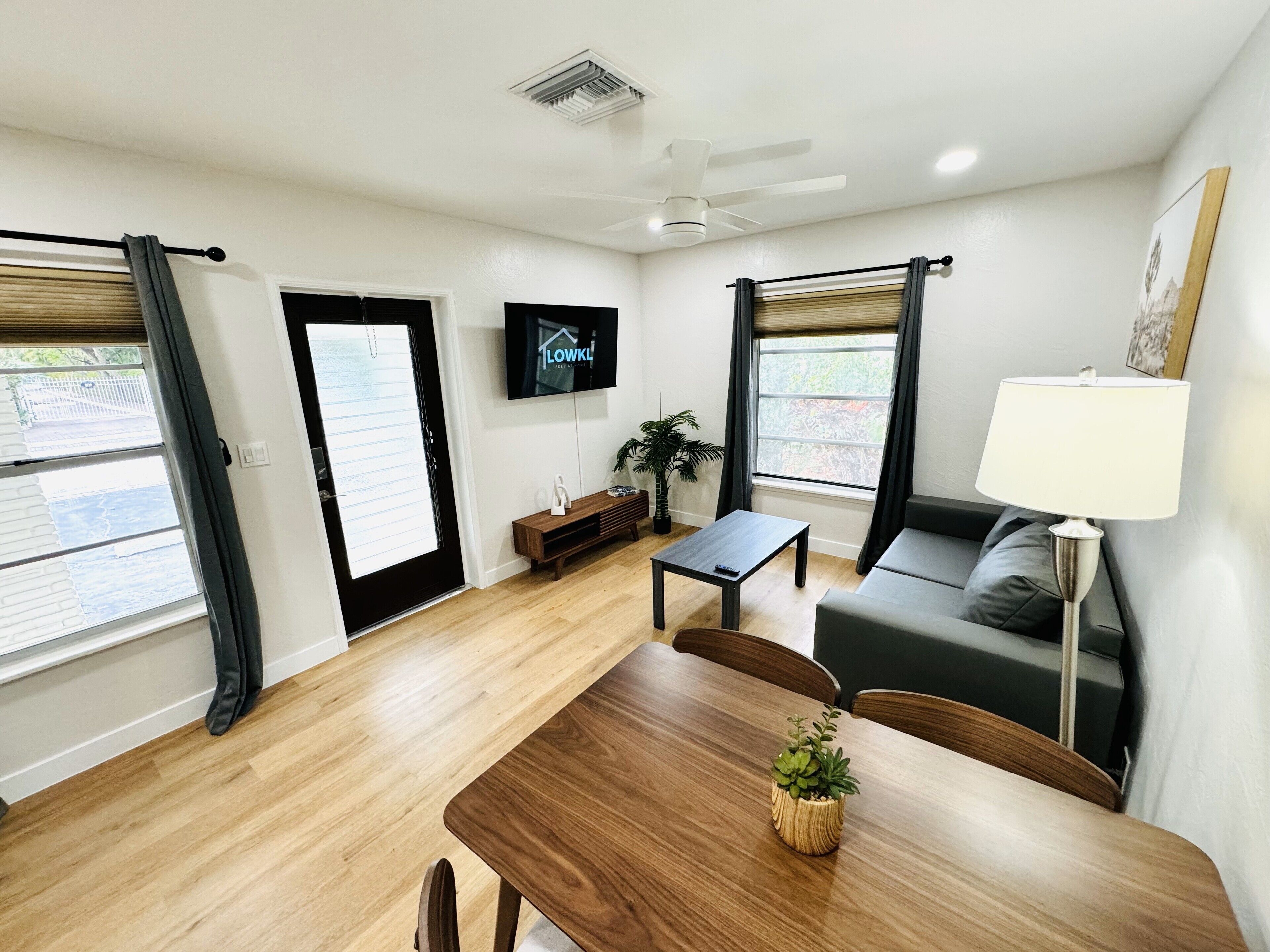 Ein modernes Wohnzimmer mit einem Holzesstisch, einer Couch, einem an der Wand montierten Fernseher und einem Deckenventilator.