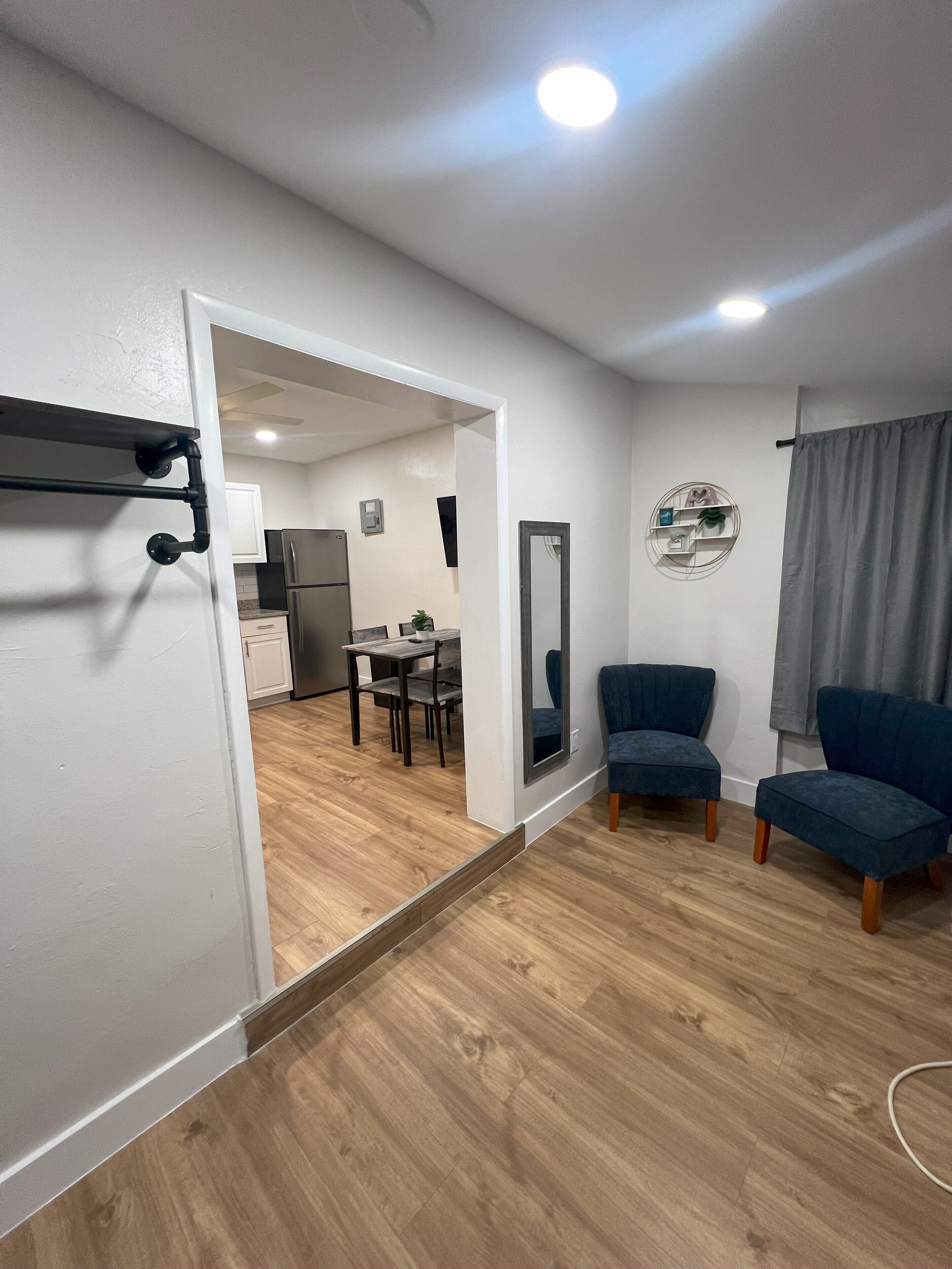 A modern apartment with a wooden floor, a dining area, a kitchen, and two blue armchairs.