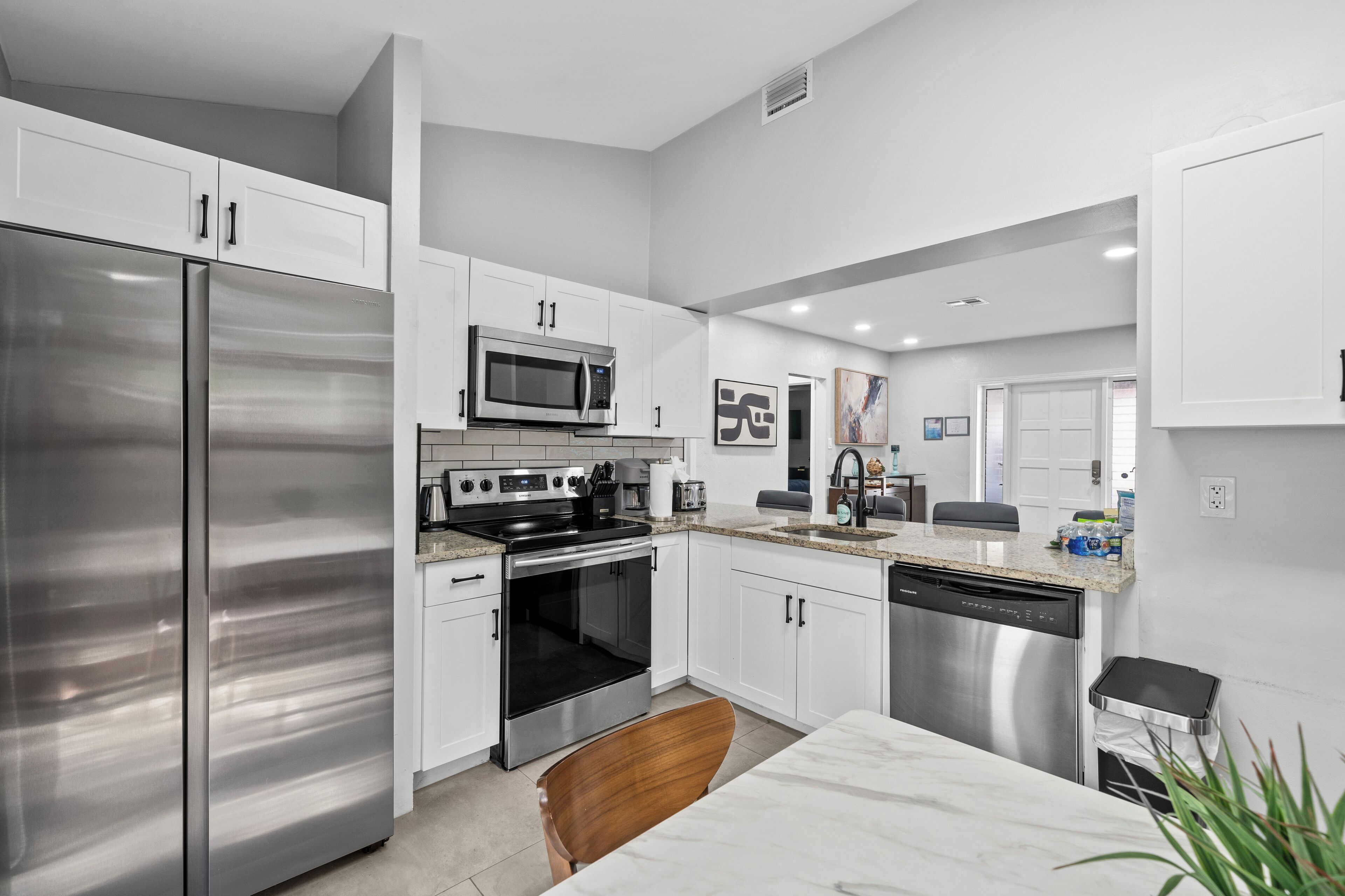 A modern kitchen with stainless steel appliances, white cabinetry, and a marble countertop.
