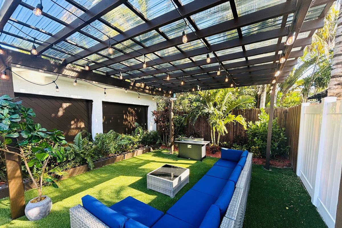 Ein überdachter Patio-Bereich mit einer langen, blauen Couch, einem Feuerkorb und verschiedenen Pflanzen.