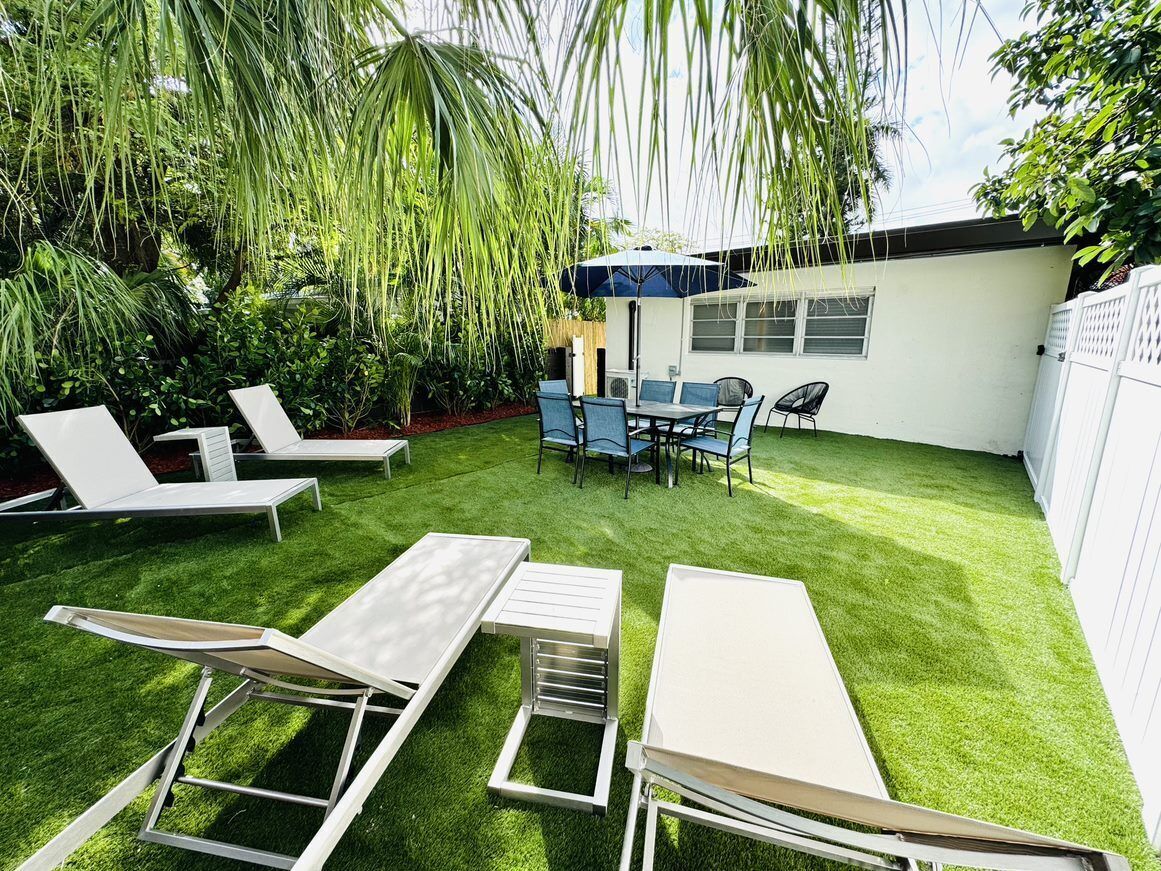 Un jardin avec une pelouse artificielle, une table à manger avec des chaises et des fauteuils de jardin.