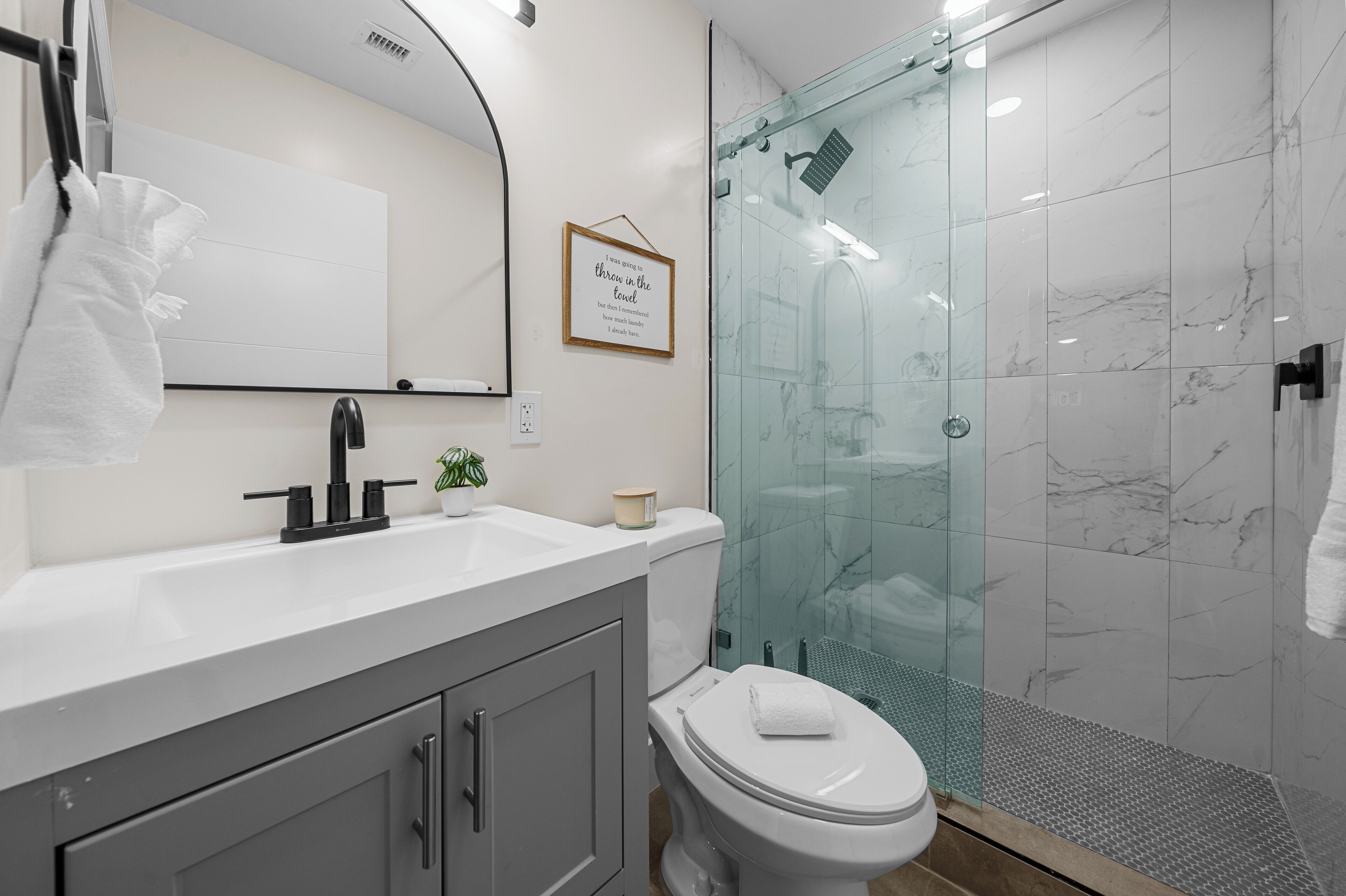 Une salle de bain moderne avec une douche à parois de verre, un lavabo blanc et une citation encadrée accrochée au mur.
