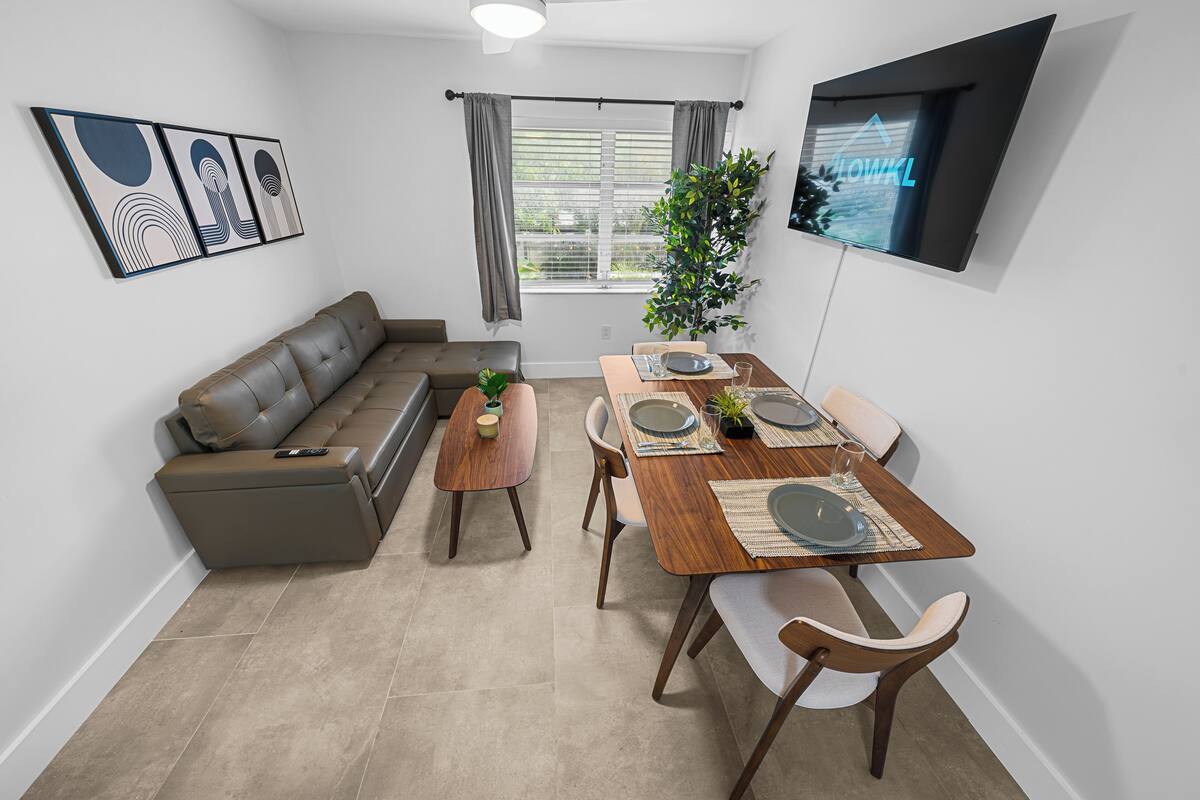 Ein modernes Wohnzimmer mit einer Couch, einem Esstisch für zwei Personen und einem an der Wand befestigten Fernseher.