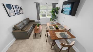 A modern living room with a sofa, a dining table set for two, and a TV mounted on the wall.