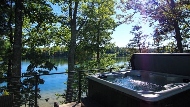 A hot tub on a deck overlooking a lake surrounded by trees.