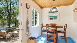A wooden deck with a table and chairs, a dog bed, and a view of a lake.