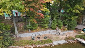 A lakeside property with a stone deck, outdoor seating, and a small cabin.
