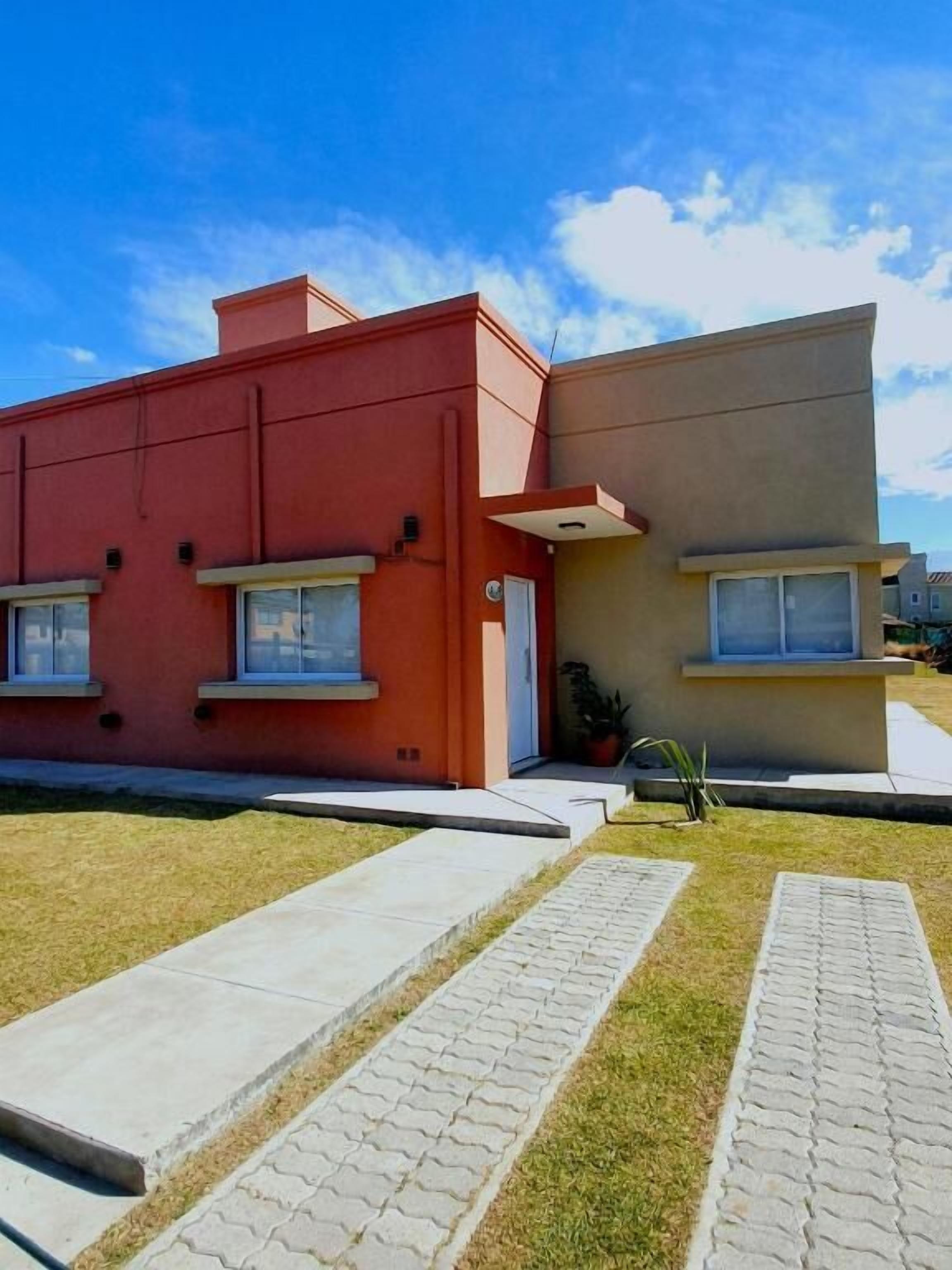 Un edificio moderno su due piani con facciata rosso e beige, ampie finestre e vialetto lastricato.