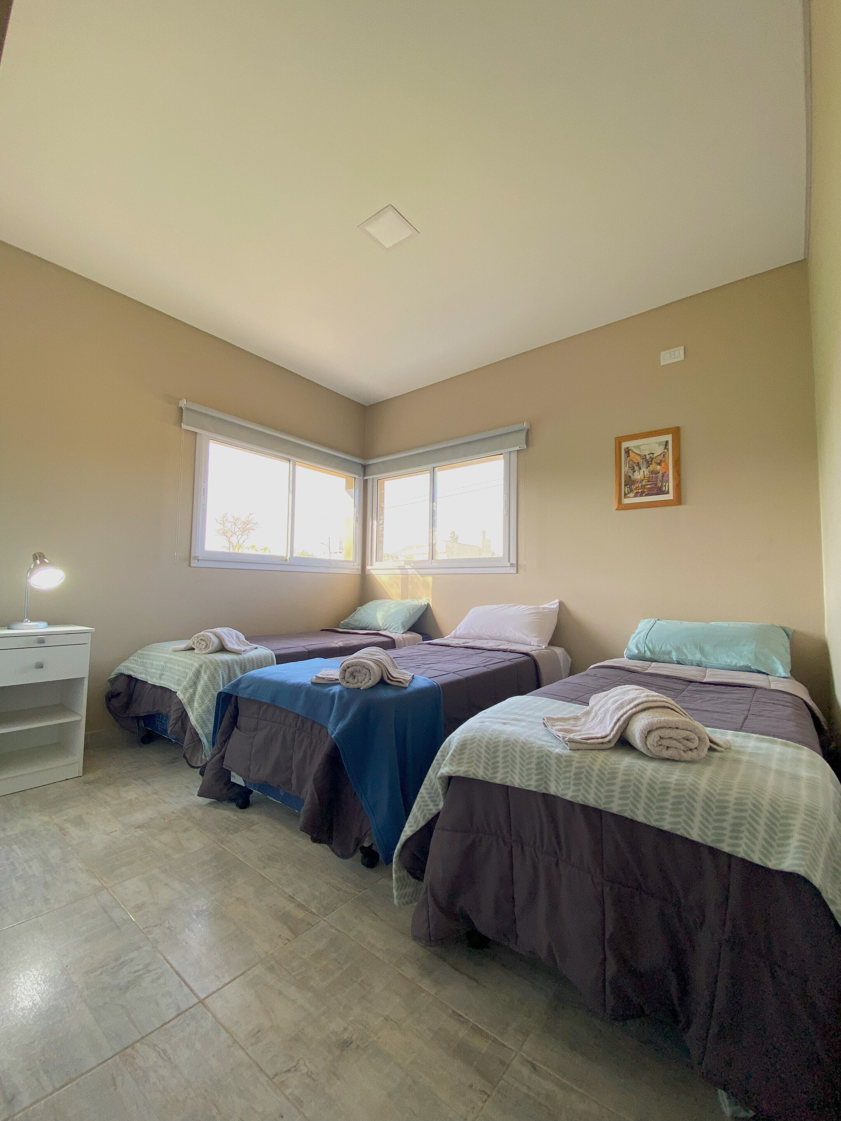 Una habitación con tres camas, un escritorio con lámpara y una ventana.