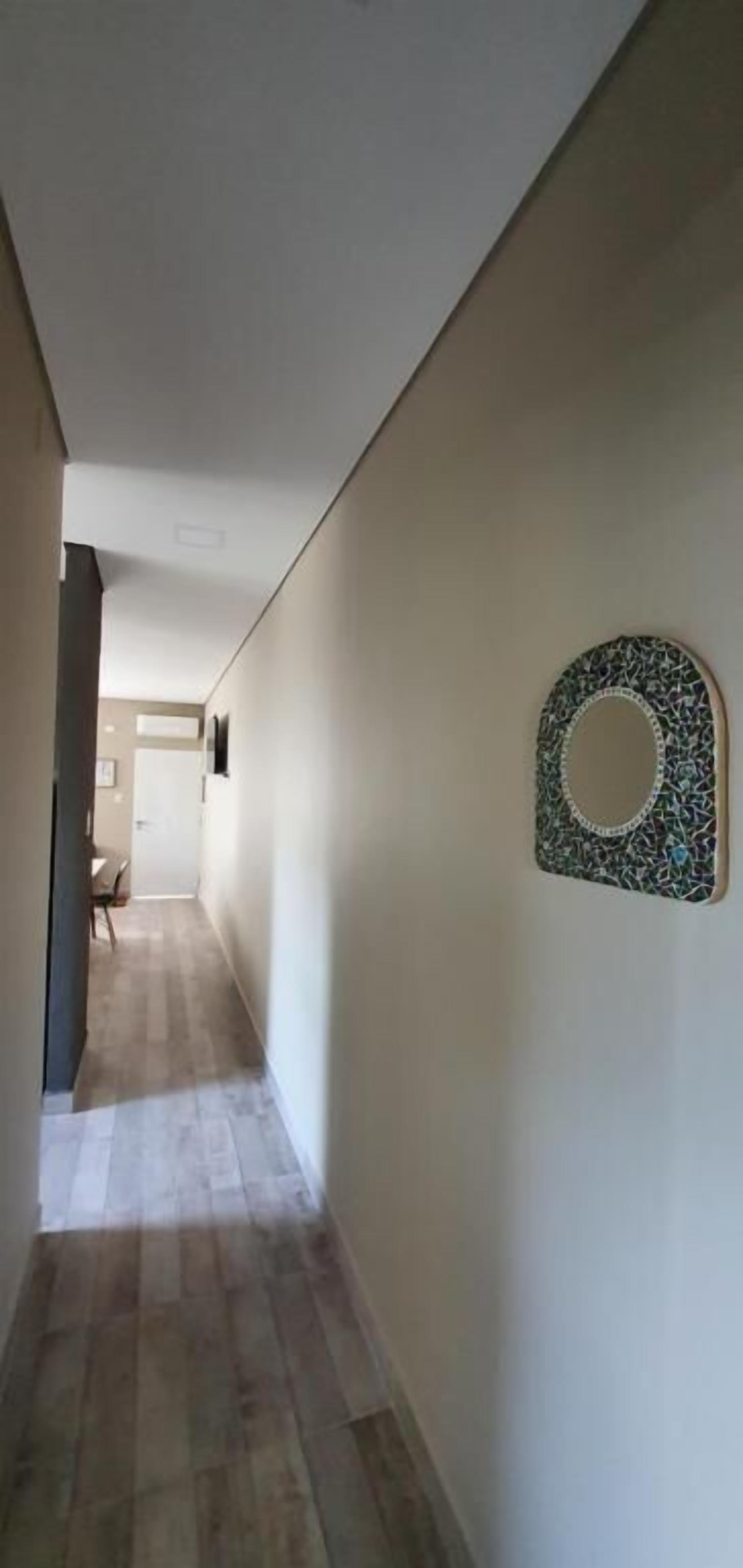 A hallway with a wooden floor and a decorative mirror on the wall.