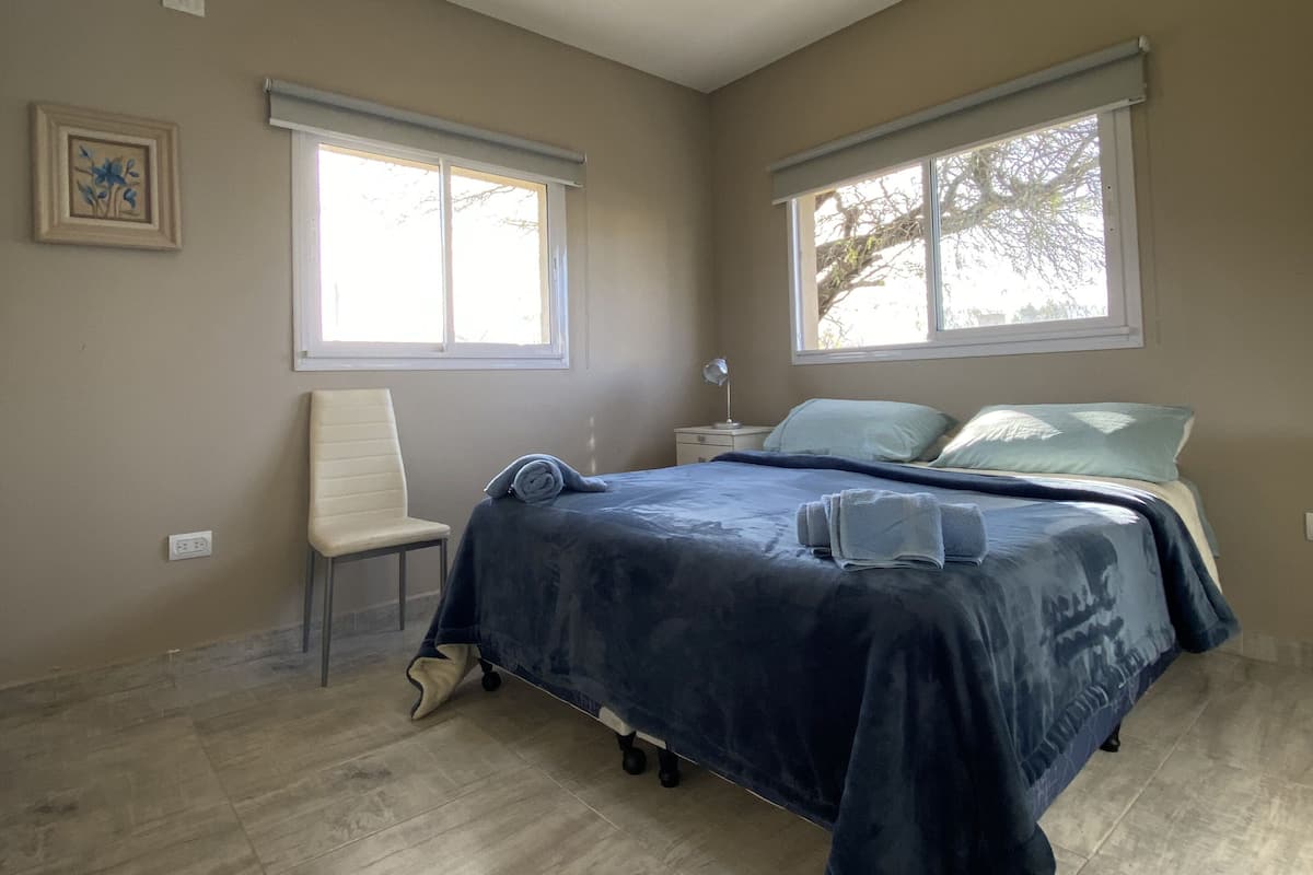 Quarto com cama, duas janelas, uma cadeira e luminária no teto.