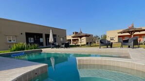 A swimming pool with clear blue water, surrounded by lounge chairs and umbrellas. - Entre Cerros Apart (Salta)