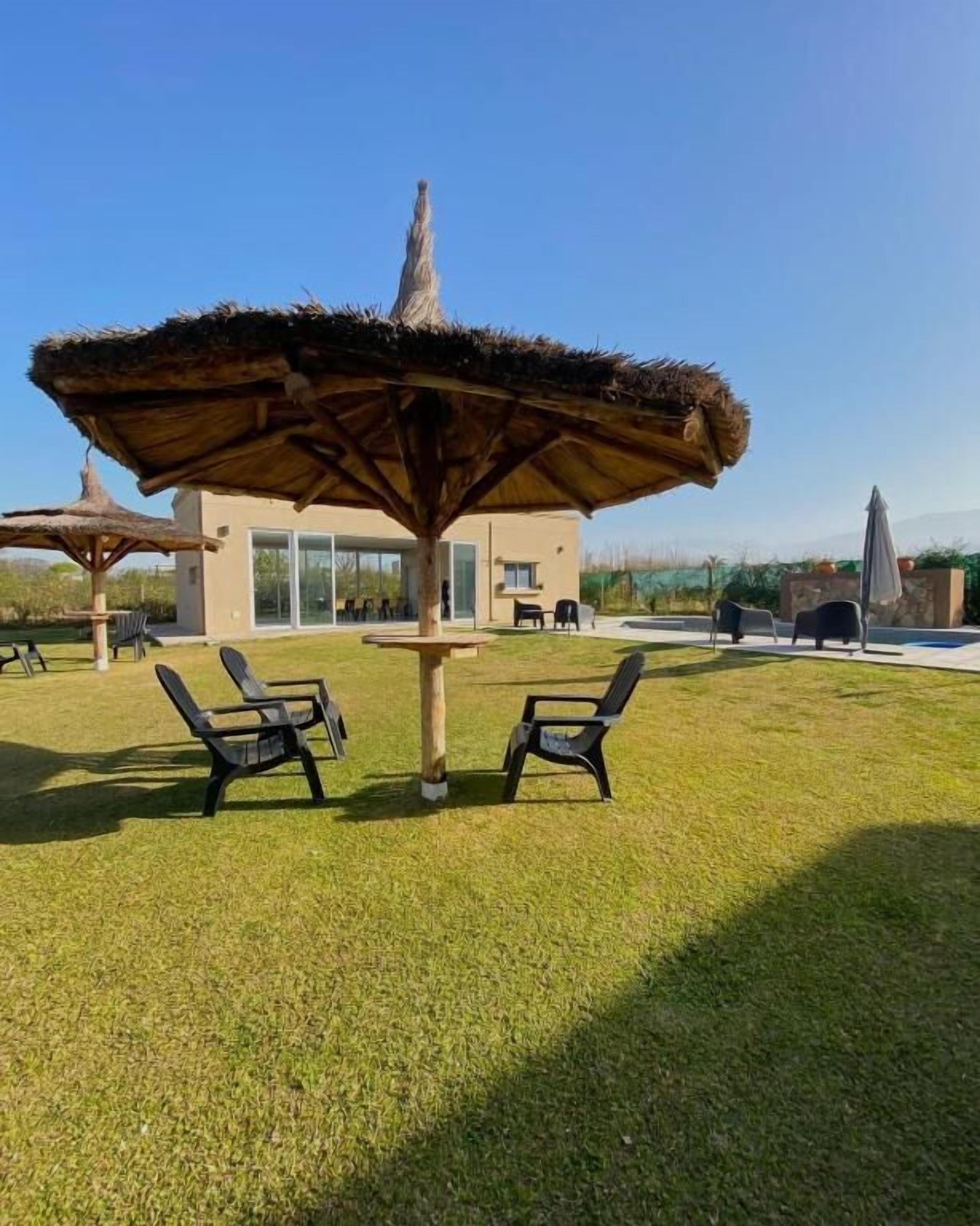 An outdoor seating area with a thatched umbrella, a modern building in the background, and a clear sky.