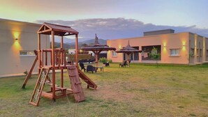 A playground with a swing set and a slide, surrounded by outdoor seating and umbrellas. - Entre Cerros Apart (Salta)