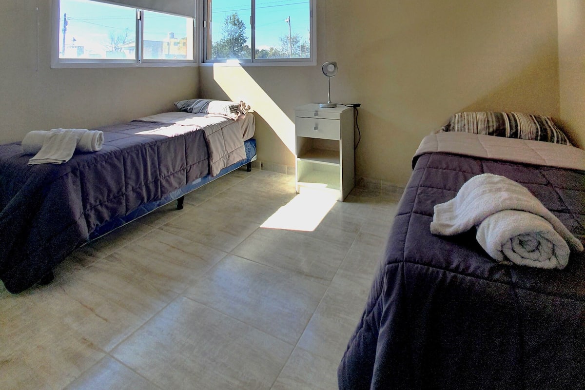 Quarto com duas camas, uma escrivaninha e uma janela.