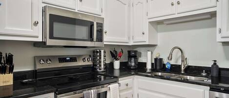 Una cocina moderna con armarios blancos, electrodomésticos de acero inoxidable y encimeras negras.