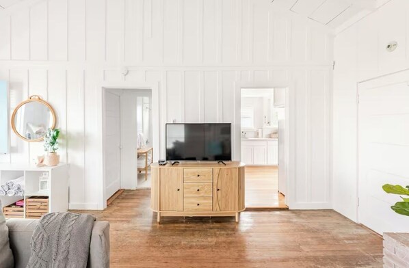 A spacious living room with a wooden cabinet, a television, and a mirror.