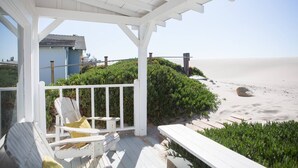 A covered outdoor area with a white pergola, a white chair, and a view of the beach. - Carpinteria Beach Front Bungalow  (Carpinteria)