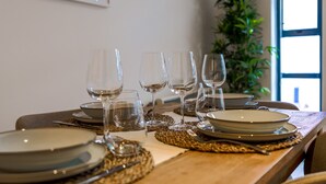 Une table à manger dressée avec des assiettes, des verres et des couverts, agrémentée d’un set de table en fibres tressées et d’une plante en arrière-plan.