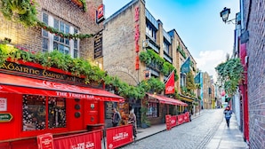 Une étroite rue pavée bordée de bâtiments en briques rouges, dont le Temple Bar, un établissement traditionnel où l’on sert de la nourriture et des boissons.
