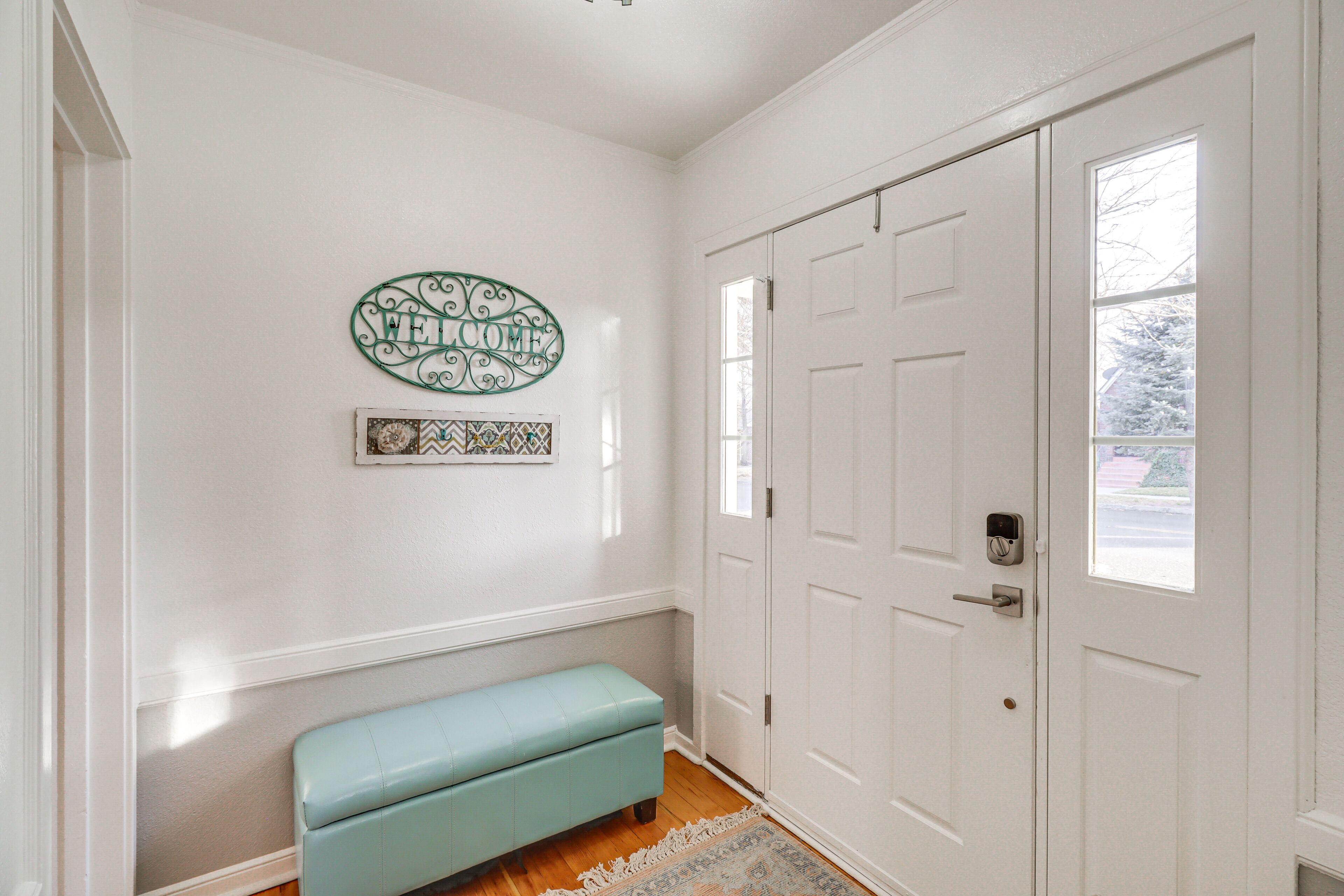 A hallway with a light blue bench, a white door, and a welcome sign on the wall.