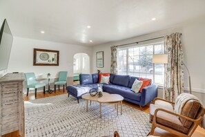 Una sala de estar con un sofá azul, una mesa de centro y un tapete estampado. Hay un comedor con dos sillas y una mesa.