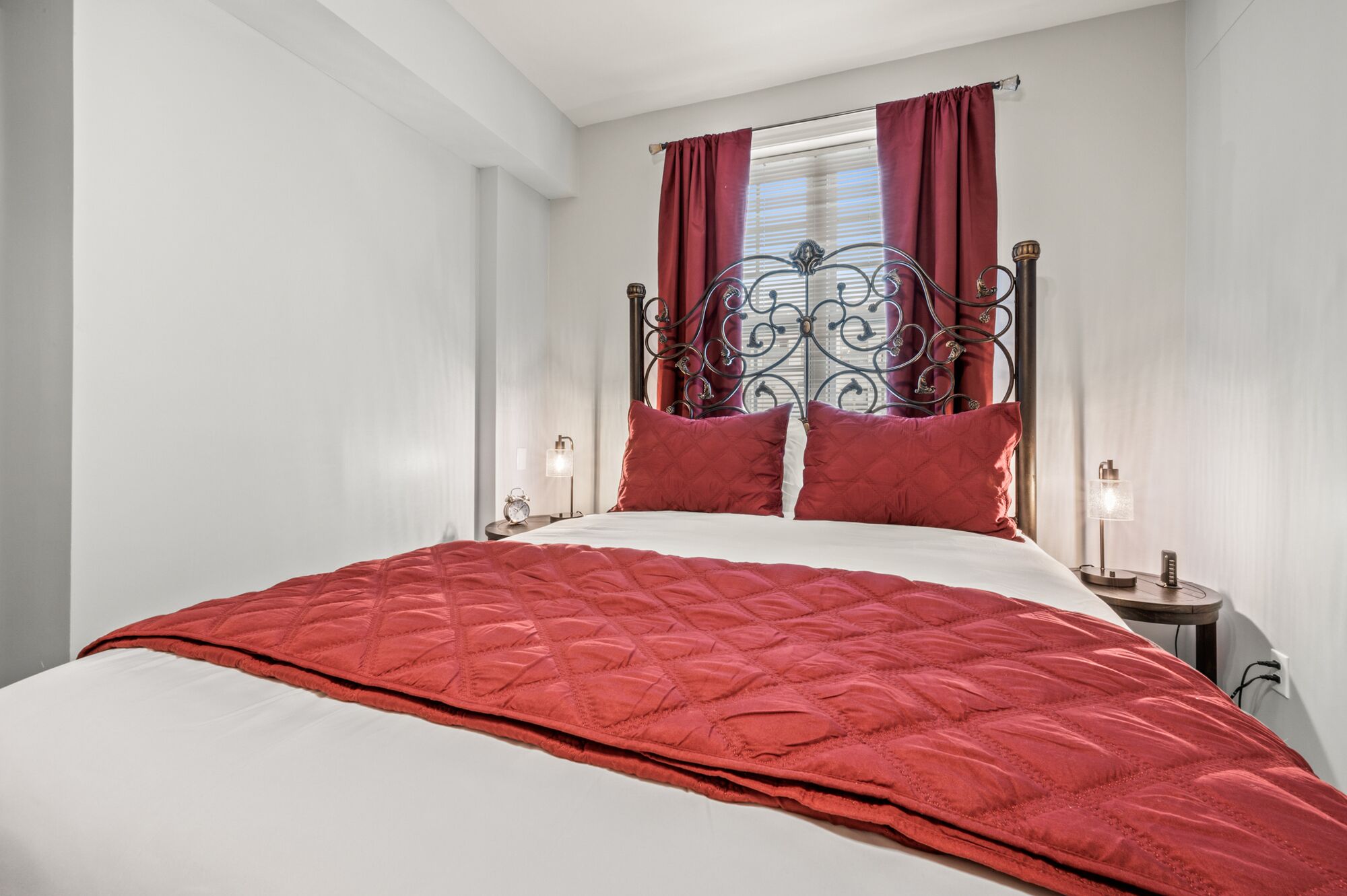 Un lit bien fait, avec une couette rouge, une tête de lit en métal et deux lampes de chevet.