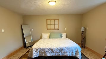 A bedroom with a bed, a mirror, a wooden floor, and a ceiling light.