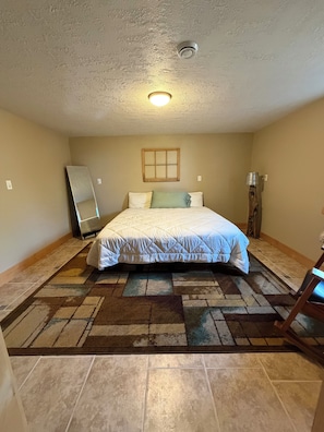 A bedroom with a bed, a mirror, a wooden floor, and a ceiling light.