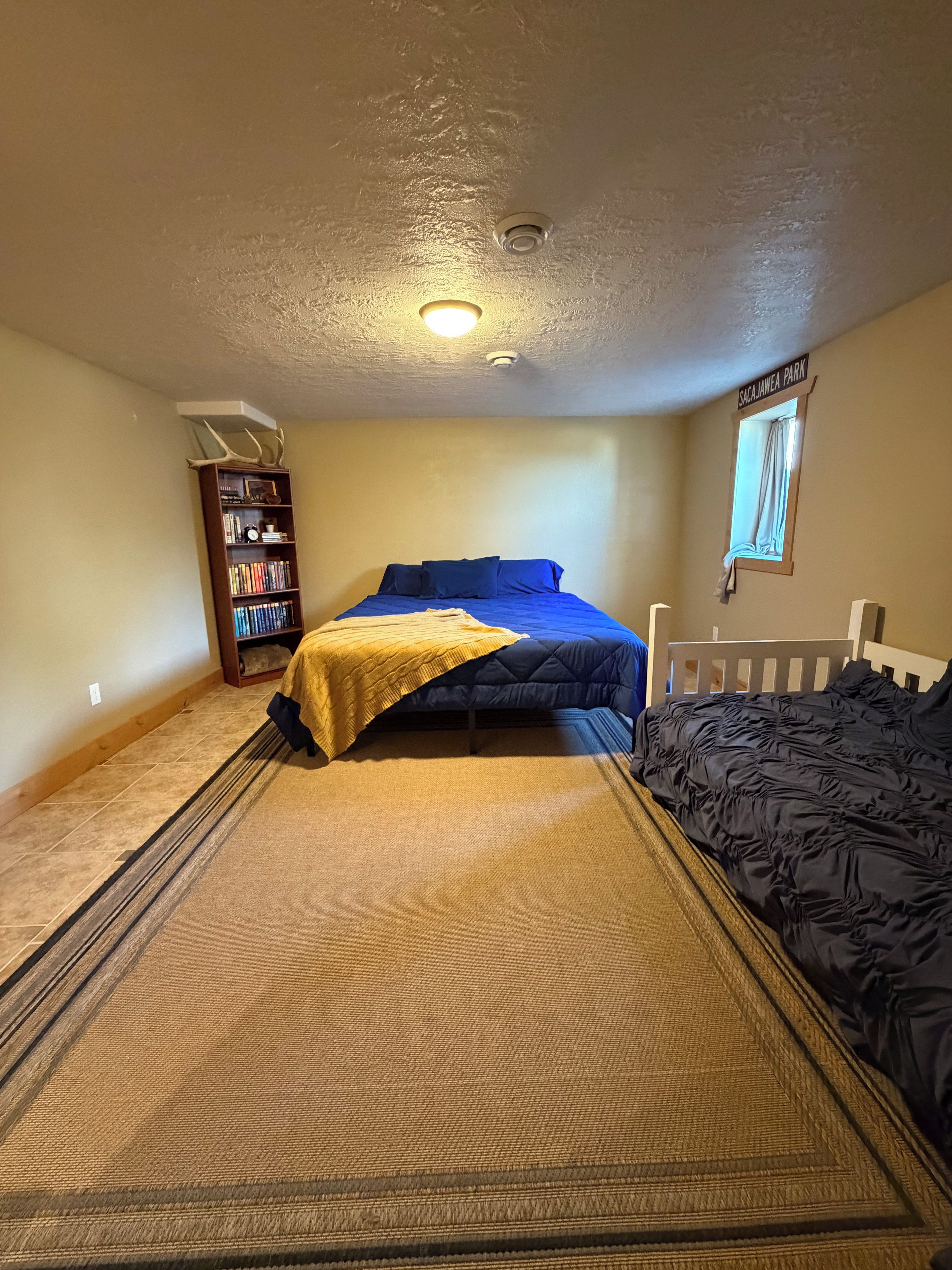 A bedroom with a bed, a bookshelf, a window, and a ceiling light.
